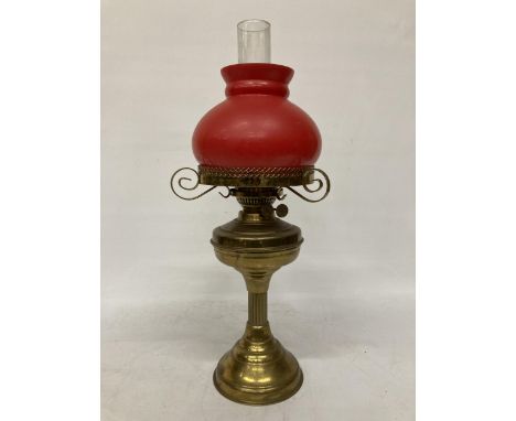A VINTAGE BRASS OIL LAMP WITH RED GLASS SHADE AND CHIMNEY, HEIGHT APPROX 55CM