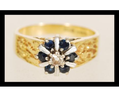 A contemporary hallmarked 18ct gold ring with six inlaid sapphires surrounding a central white stone in a decorative setting 