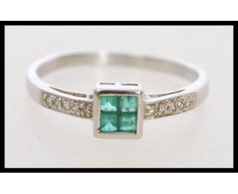 A hallmarked 9ct white gold Art Deco style emerald and diamond ring set with four central square cut emeralds, and diamond se