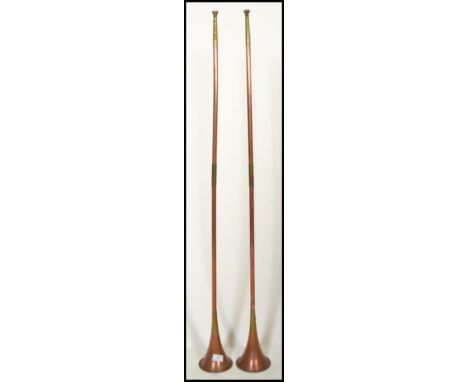 A pair of long early 20th century copper and brass banded hunting horns of tapering form with mouth pieces.