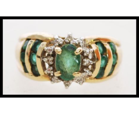 A hallmarked 14ct gold ring set with a central oval cut emerald with diamond halo having emeralds to the shoulders. Weight 3.