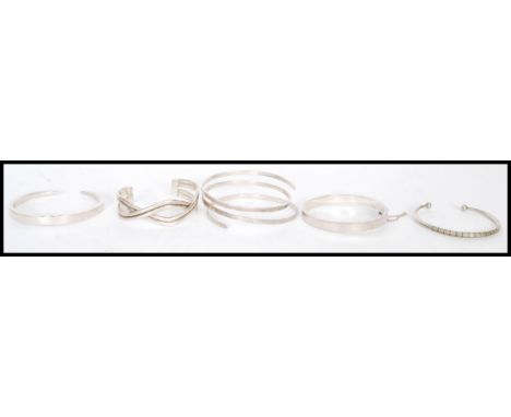 A selection of silver bangles, one having a hinged opening and safety chain, a bangle with geometric engraving and a crossove