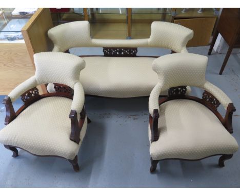 An Edwardian mahogany and upholstered salon suite comprising sofa and two armchairs, with cream foliate upholstery and carved
