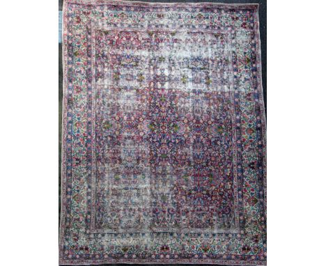 A Kirman ivory ground carpet, with polychrome field of scrolling foliage and five row foliate border,