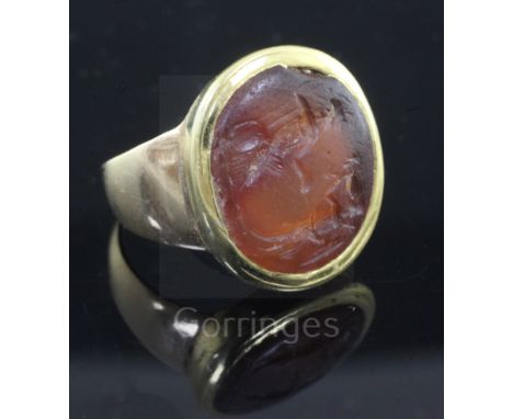 An antique gold mounted Roman? intaglio carnelian ring, of oval shape, caved with two figures (worn), size L.