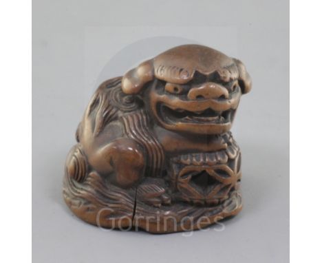 A Japanese wood netsuke of a shishi, seated on a rock, 19th century, its paw and chin resting upon a brocaded ball, two chara