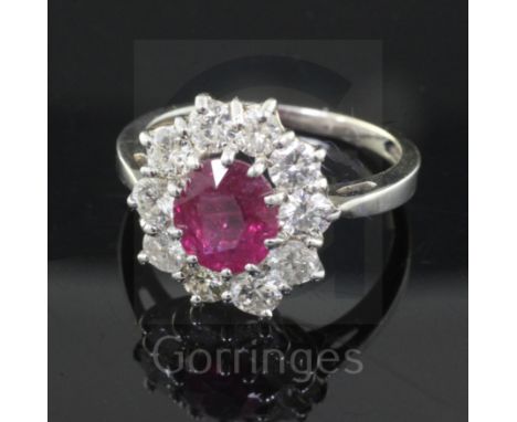 A white gold, ruby and diamond cluster ring, the oval cut central ruby bordered by ten round brilliant cut diamonds, size O.