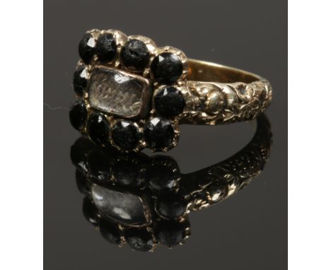 A 19th century paste set mourning ring with a hair plait panel and chased shoulders, size M. 