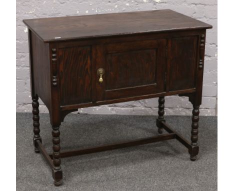 A carved oak and panelled cupboard raised over bobbin turned legs. 