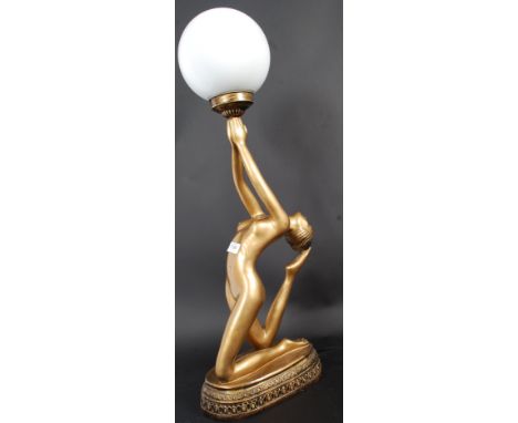 A 20th century contemporary table lamp of an art deco lady in gold having milk glass shade to her hands being raised on a pli