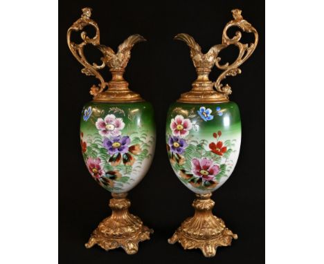 A pair of Rococo Revival gilt-metal mounted ewers, the ovoid ceramic ewers painted with country flowers in tones of polychrom