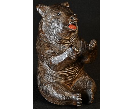 A Black Forest novelty inkwell, carved as a bear, seated, smiling, glass eyes, painted mouth, hinged cover enclosing a glass 