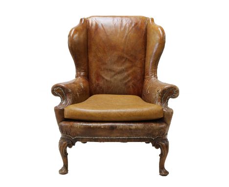 A Queen Anne-style leather wingback armchair,first half of the 20th century, with studded detail and raised on four walnut ca