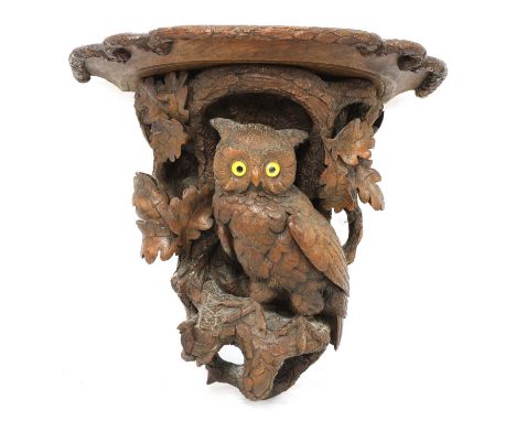 A Black Forest carved softwood wall bracket,late 19th century, the shaped shelf above an owl with glass eyes perched amongst 