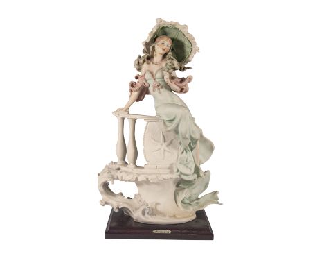 Hand decorated figure of a long hair beauty seated on a balcony railing with an umbrella over her head. Crashing waves are se