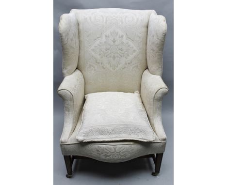A GEORGIAN DESIGN WING BACK ARMCHAIR having ivory damask effect all over upholstery with extra cushion, supported on four squ
