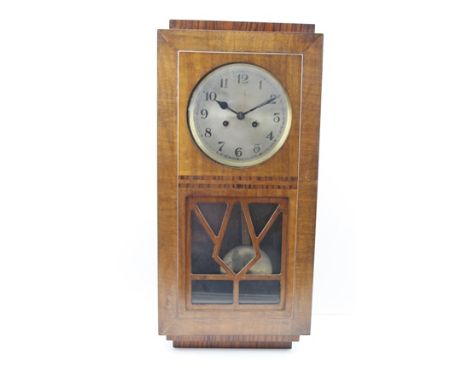 AN ART DECO WALNUT VENEERED WALL CLOCK, the glazed door with decorative glazing, the circular dial with Arabic numerals, 8-da