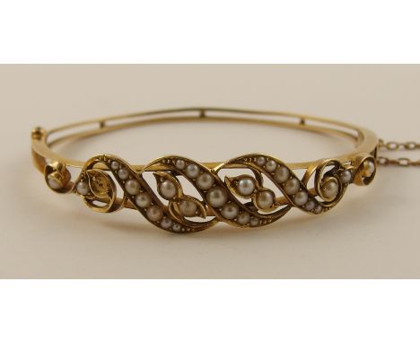 An Edwardian pearl set bangle of floral theme in yellow metal, with knife edge and spacer reverse. Approx weight 13.2gms.