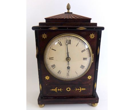 A Regency mahogany and brass inlaid mantle clock with pine cone finial on a fluted splayed hood above a convex painted Roman 