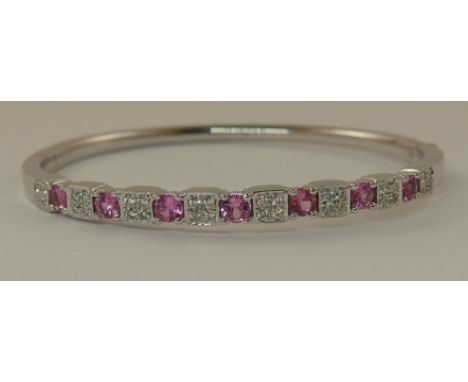 An 18ct white gold pink sapphire and diamond bangle the seven 3.4mm round facet cut sapphires are interspaced with panels of 