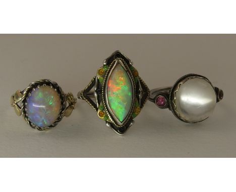 Three arts and crafts style rings comprising of a yellow and white metal ring set with a marquis shaped opal with good red/bl