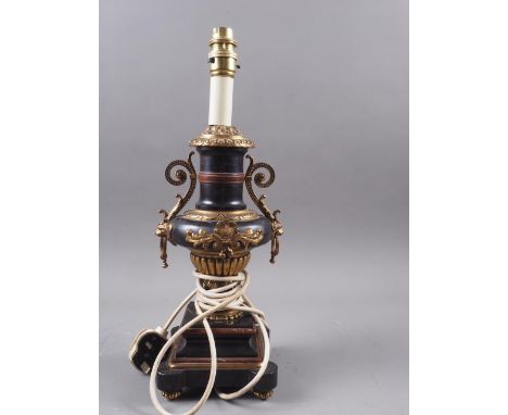 A black marble urn shaped table lamp with scrolled handles and crimson and gilt highlights, on four fluted padded supports, 1