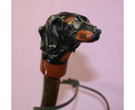 An ash shank walking stick with leather wrapped handle and thong and painted carved Daschund like dog head. Overall length 12