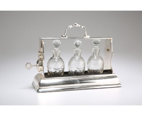 AN EDWARDIAN SILVER-PLATED THREE-BOTTLE TANTALUS, the locking mechanism complete with key, the three cut-glass bottles with t