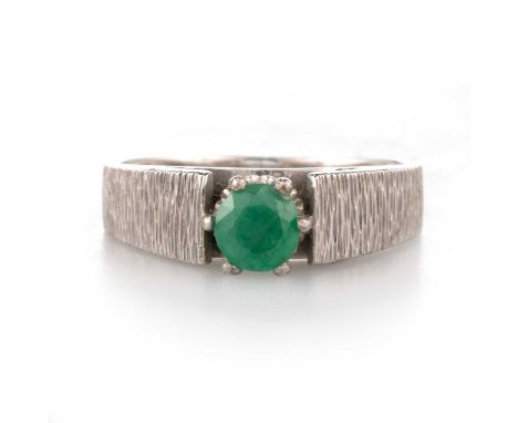 A SOLITAIRE EMERALD RING a round-cut emerald to textured tapering shoulders. Marked '18CT', ring size M1/2, 4.2 gramsLight we