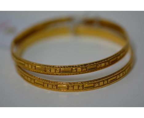 A pair of Indian yellow metal bangles, unmarked but test as 22ct gold, each decorated with star and baton motifs on a texture