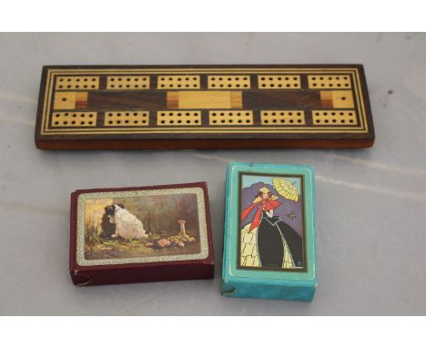 A Victorian marquetry cribbage board, parquetey inlaid, complete with two packs of playing cards (3)