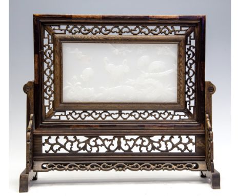 A Chinese wooden table screen, fret craved and inset with a white jade tablet carved in relief with storks, height 33cm, widt