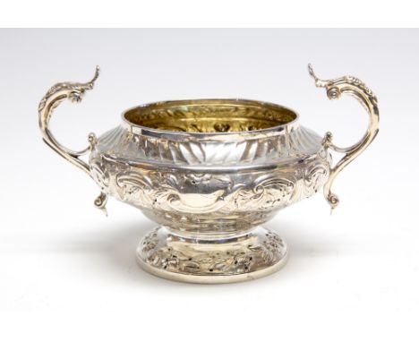 A George IV shaped circular two handled sugar basin, chased with scrolling mid section beneath wyvern rim, open scroll handle