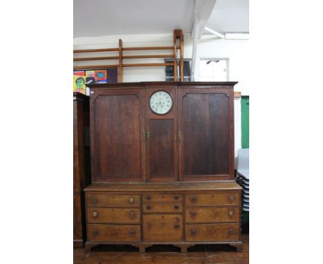 A George III oak House Keepers cupboard with clock to centre, the eight day clock with a white enamelled dial and black Roman