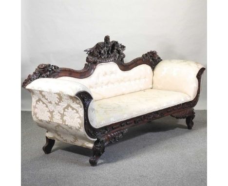 A 19th century style carved and cream upholstered sofa, the undulating back centred by an eagle, with scrolled arms, on cabri