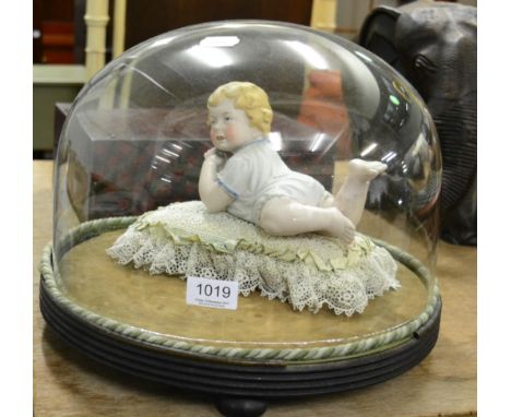 A German bisque piano baby ornament, on lace cushion, glass dome and ebonised base 
