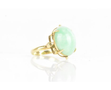A Chinese jadeite yellow gold dress ring, the oval jadeite cabochon 17.2mm x 12.8mm, in a four claw setting with pierced scro
