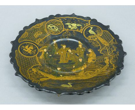 A Japanese Meiji period black lacquered pedestal dish with barbed rim decorated in gold with an Imperial court scene and Budd