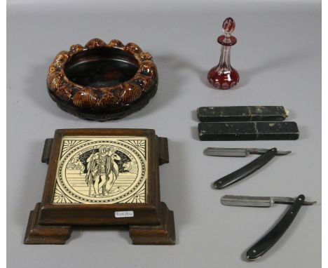 A Victorian Minton tile in oak mount, a treacle glazed pottery spittoon, two cut throat razors and a ruby glass bottle and st