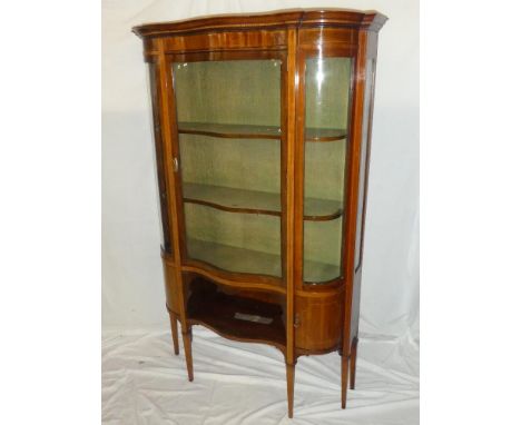 A late Victorian inlaid mahogany serpentine fronted display cabinet with fabric lined shelves enclosed by a curved glazed doo