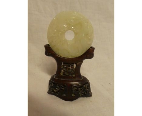 A Chinese jade circular panel decorated in relief with a dragon, 2¼" diameter on carved wood stand