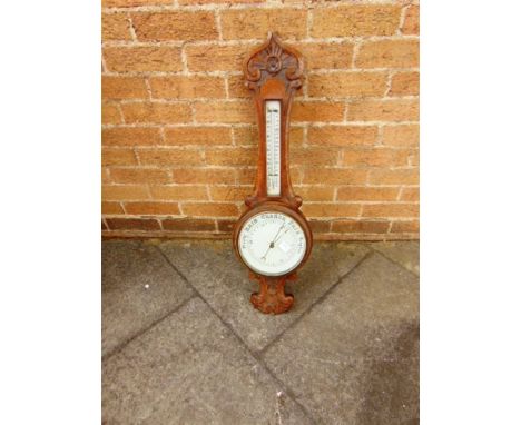 AN EDWARDIAN CARVED OAK ANEROID BAROMETER/THERMOMETER the white ceramic dial 20cm diameter, 84cm high overall