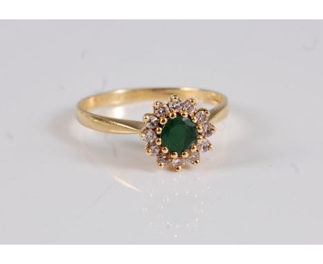 An 18ct emerald and diamond cluster ring, the round emerald, surrounded by small round diamonds, total estimated approx. 0.12