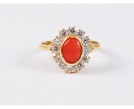 An 18ct coral and CZ ring, the oval coral cabochon, 7.8mm long, in rubover mount, surrounded by round CZ's, all set in yellow