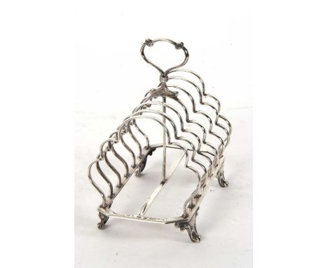 A large Victorian silver toast rack having six shaped divisions, central loop carrying handle, supported on four cast scrolle