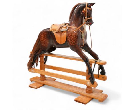 Carved wooden rocking horse, painted in dapple brown with glass eyes, fitted with tan leather saddle and stirrups, on oak tre
