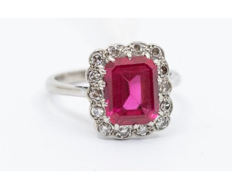 An Art Deco synthetic ruby and diamond set platinum ring, the central claw set rectangular stone within a border of  eight cu