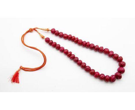 A carved ruby  bead necklace, comprising a single row of oval earth-mined carved ruby beads, on a decorative cord and tassel 