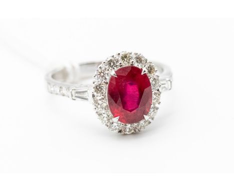 A ruby and diamond 18ct white gold halo cluster ring, the centre claw set with an oval ruby weighing approx 2.88 carats, with