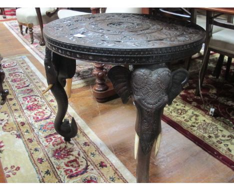 AN ORIENTAL HARDWOOD TABLE of circular outline the shaped moulded top carved with flowerheads, foliage and figures raised on 